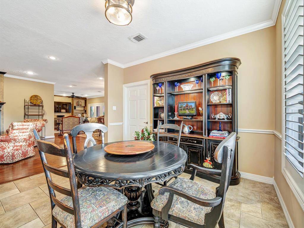 This inviting dining area features a round table with ornate chairs, a large decorative hutch, and warm beige walls. The space opens into a cozy living room with hardwood floors, offering a seamless flow for entertaining.