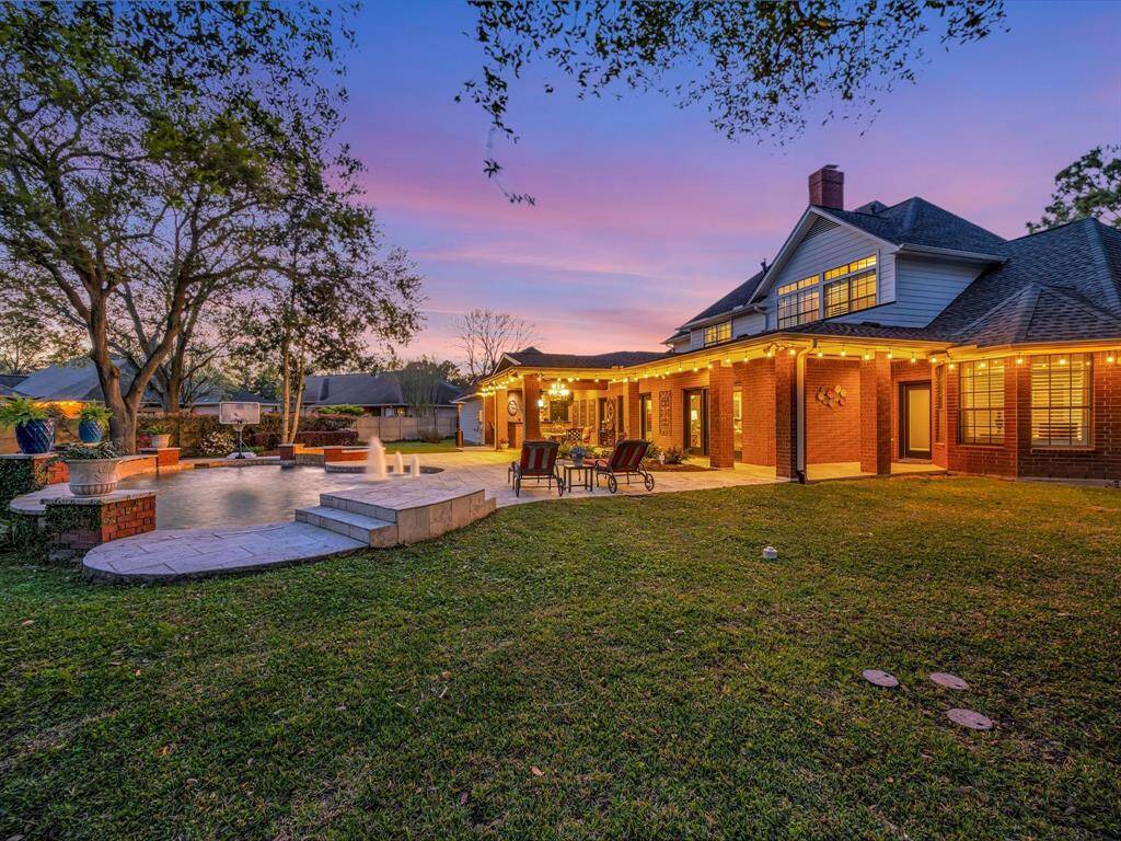 This stunning backyard features a spacious patio with elegant string lights, a beautiful swimming pool with water features, and lush landscaping, perfect for entertaining and relaxation at sunset.