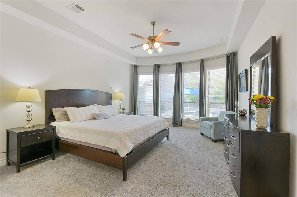 The generous primary bedroom, with its trayed ceiling and ceiling fan, has enough space for a king size bed and a sitting area in front of the bow windows. Full curtains frame the view of the pool.