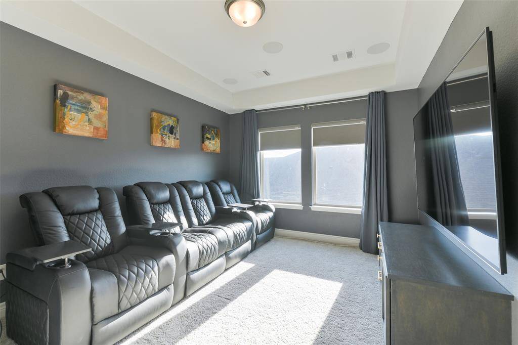 Media room has built-in cabinet, room darkening shades, trayed ceiling with surround sound speakers.