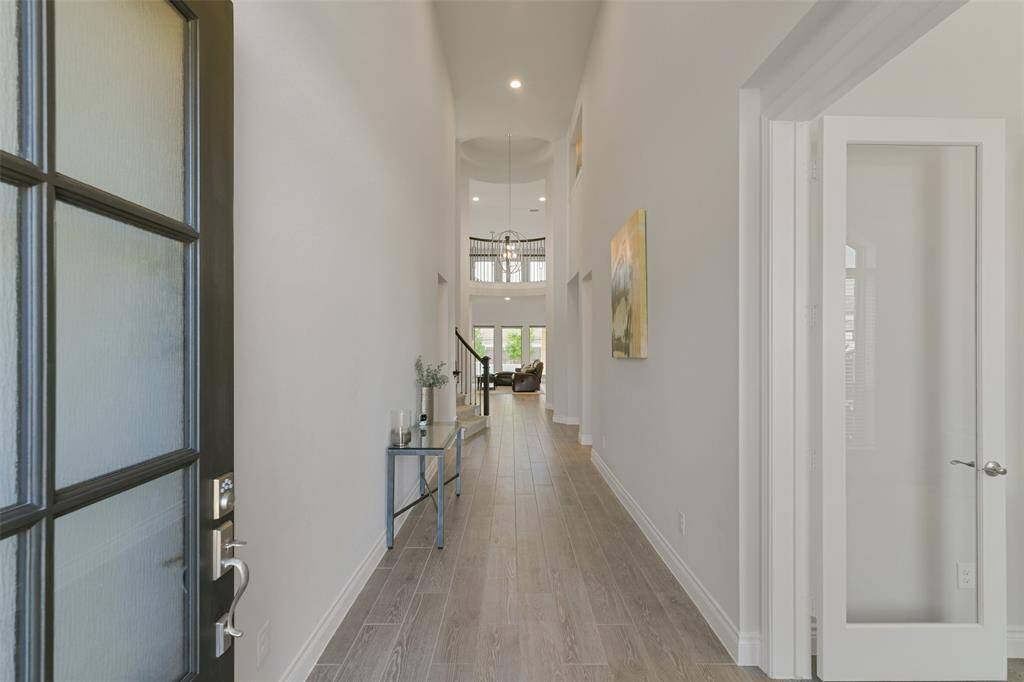 This impressive entry opens to high ceilings, ceramic wood look tile floors, and the entrance to the study to the right. Looking to the back, you can see the wall of windows with a view to the pool.