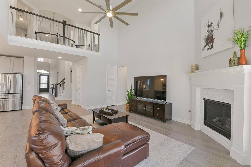 Balcony above with iron spindles overlooks entry and family room with corner fireplace.