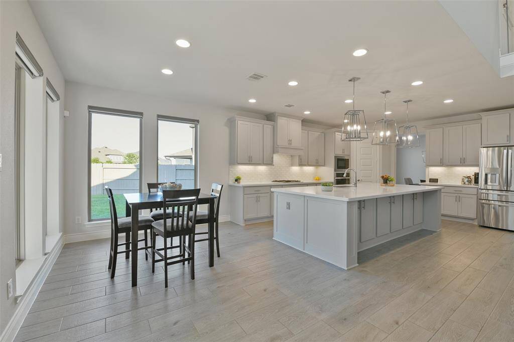 Breakfast room is surrounded by windows with remote shades. Ceramic wood look tile flows throughout this space. The enormous kitchen has cabinets to spare, even under the oversized island and breakfast bar. In addition to all the natural light flooding this space, ample LED lighting, pendant lights, and undercabinet lighting make the kitchen so light and bright.