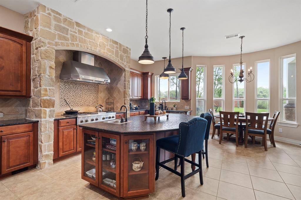 Gourmet kitchen features a spacious island with bar seating, custom stonework, and a cozy breakfast nook surrounded by stunning panoramic windows.