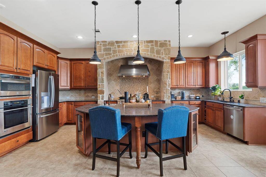 Chef’s dream kitchen with built-in stainless steel appliances, rich wood cabinetry, and a grand stone arch over the gas range.