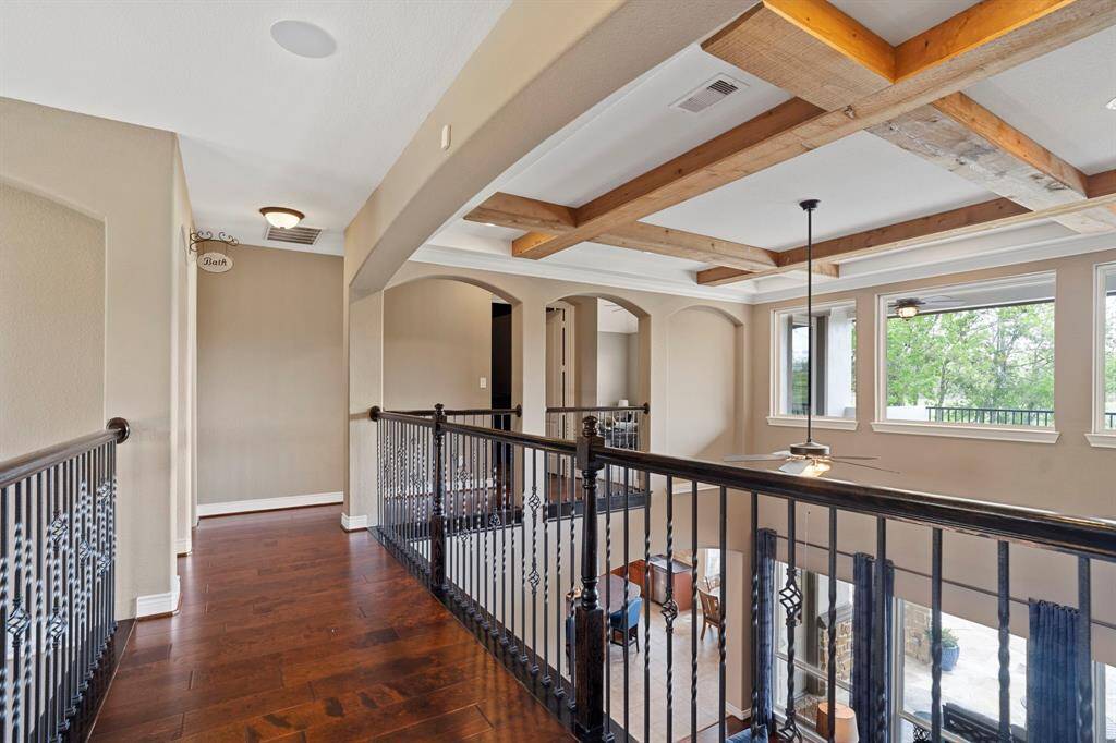Stunning upstairs landing with hardwood floors, wrought-iron railings, and exposed beam ceiling overlooking the living space below.
