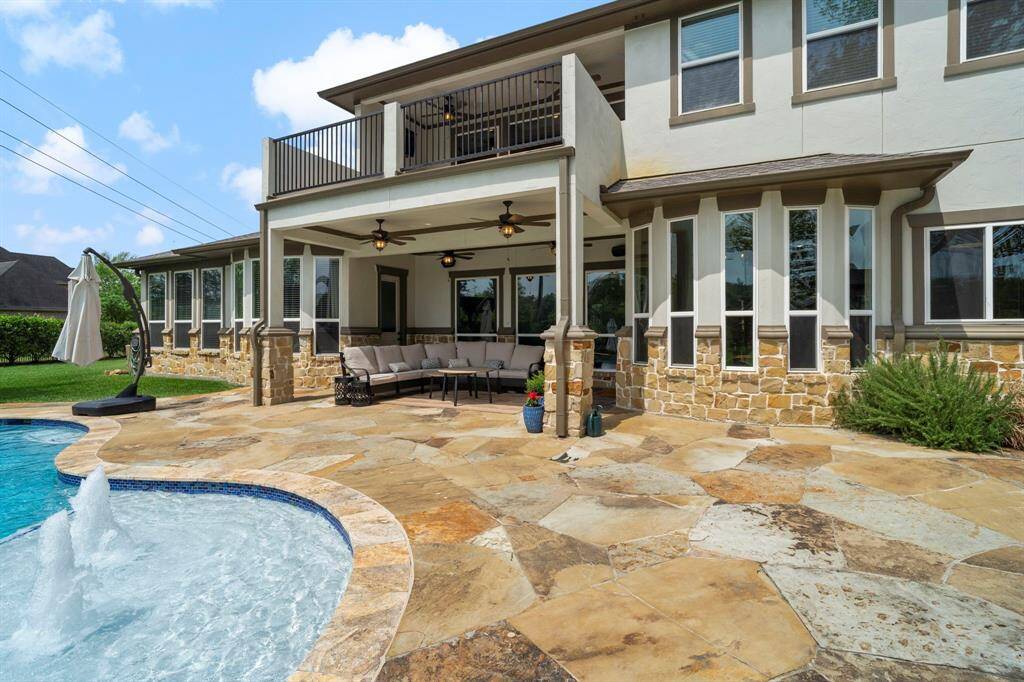 Expansive flagstone patio with covered seating, ceiling fans, and easy access to the pool—ideal for outdoor living and entertaining.