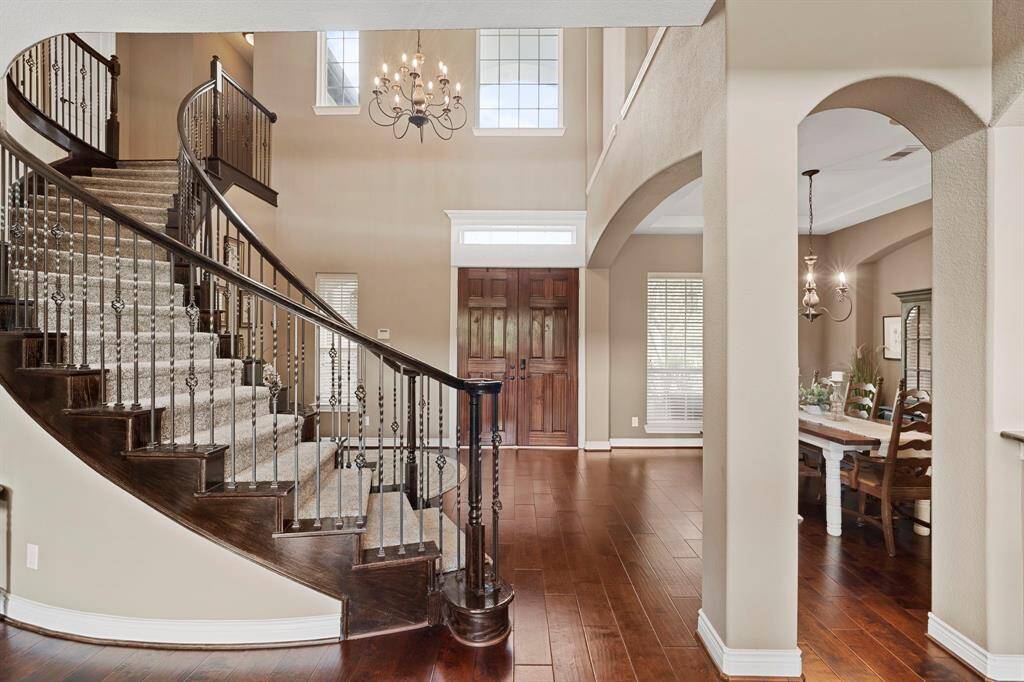 Stunning grand entryway featuring a sweeping staircase, elegant chandelier, and rich hardwood floors.