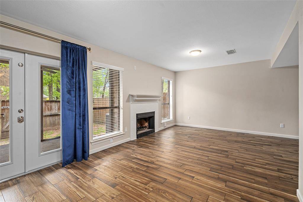 Your inviting living room features rich wood looking tile flooring, a cozy fireplace, and ample natural light from large windows. French doors lead to the outdoor space, creating a seamless indoor-outdoor flow.
