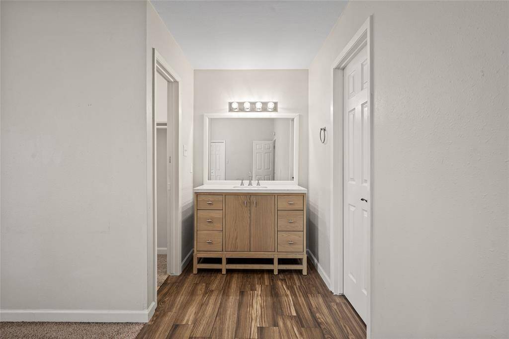 Your modern bathroom vanity area spotlights an updated wooden cabinet with a sink, a large mirror, and overhead lighting. The space has a clean design with neutral walls and wood look tile flooring offering a simple and functional style.