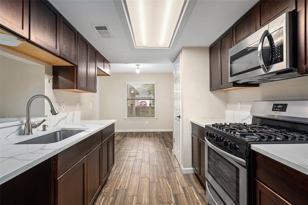 Your new kitchen features modern stainless steel appliances, updated dark wood cabinetry, and quartz countertops. The tile flooring adds warmth, and a window provides natural light.