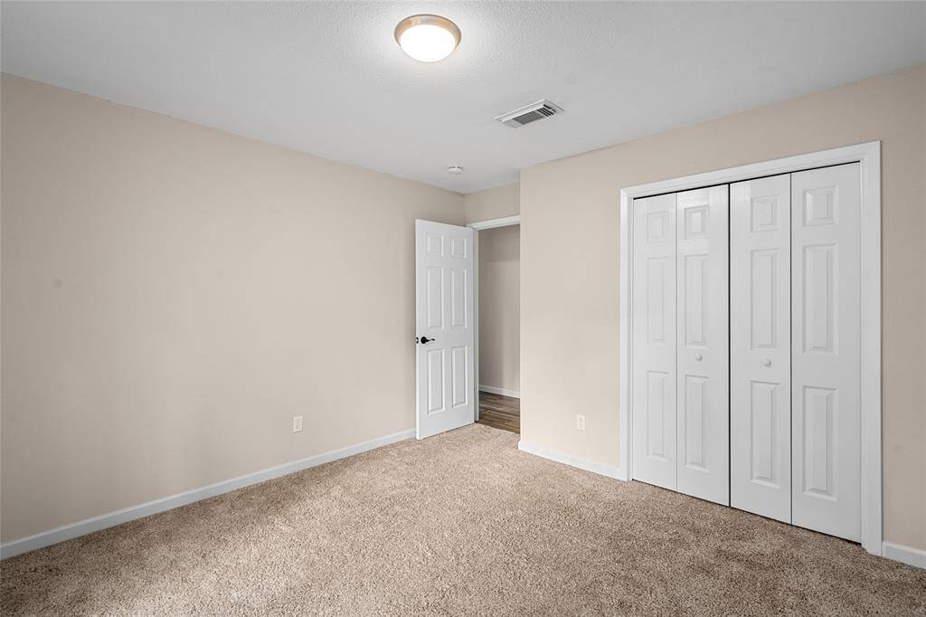 This is a bright, neutral-toned bedroom with carpeted flooring. It features a ceiling light and a closet with double doors.