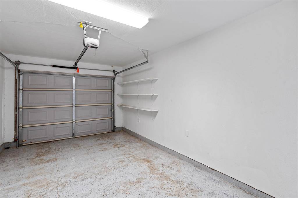 Your single-car garage is equipped with automatic opener. It features white walls and wall-mounted shelves for storage.