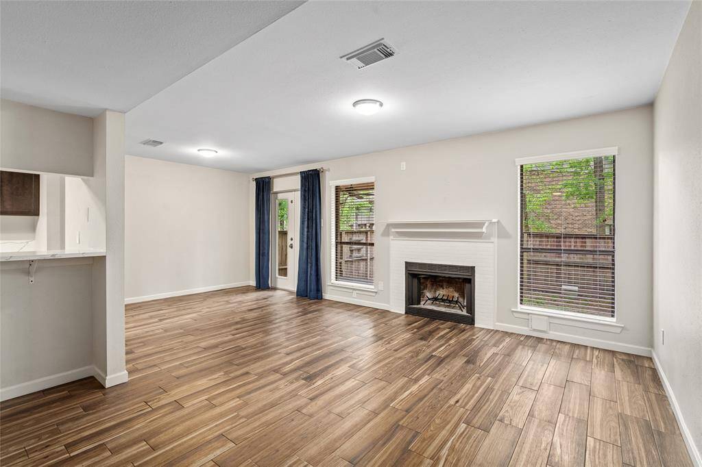 Your new spacious living area features wood-look tile flooring, a cozy fireplace, and ample natural light from large windows. It opens to a small patio through French doors, perfect for indoor-outdoor living.