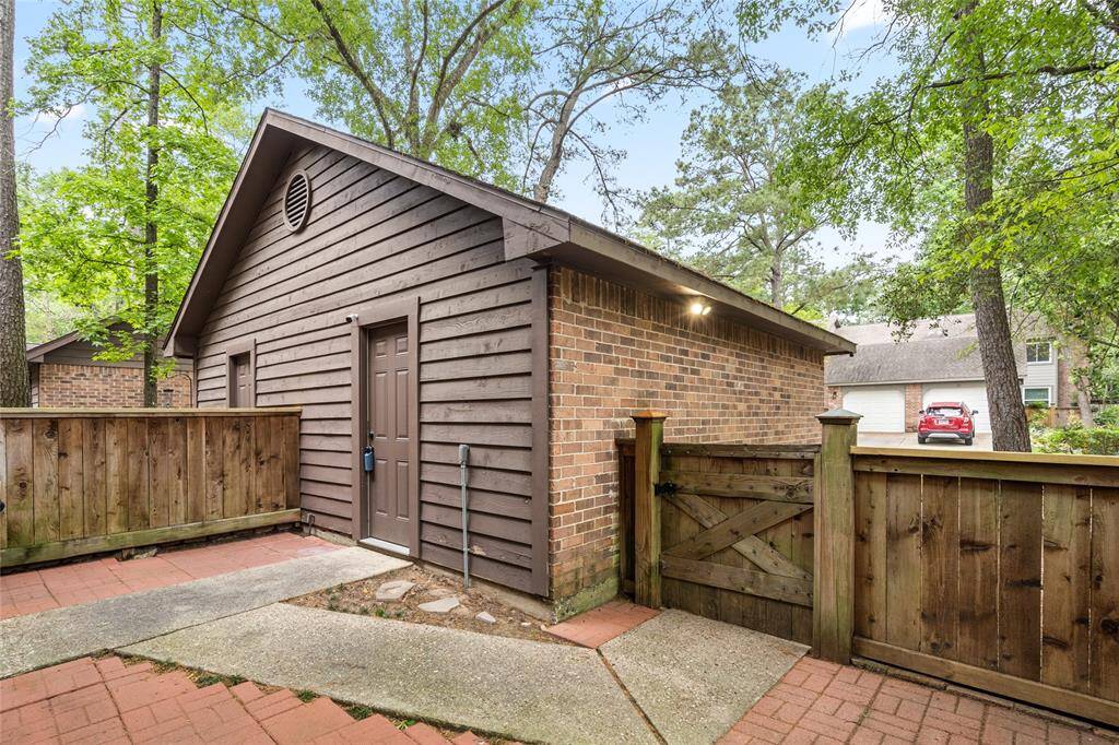 The back side of your garage has a combination of brick and wooden exterior. It features a secure wooden fence and gate set on a red brick and concrete pathway and is surrounded with mature trees for a tranquil, natural setting.