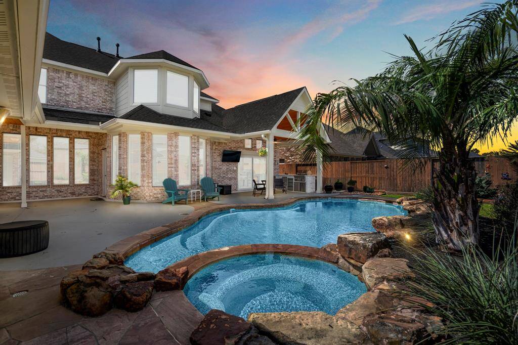 This breathtaking backyard retreat features a sparkling pool with a built-in spa, surrounded by natural stone accents and lush tropical landscaping. A covered patio and outdoor kitchen create the perfect setting for entertaining, while the expansive pool deck offers ample seating to enjoy the serene sunset views. With high-end finishes, privacy fencing, and elegant architectural details, this space embodies luxury outdoor living in the heart of Gleannloch Farms.