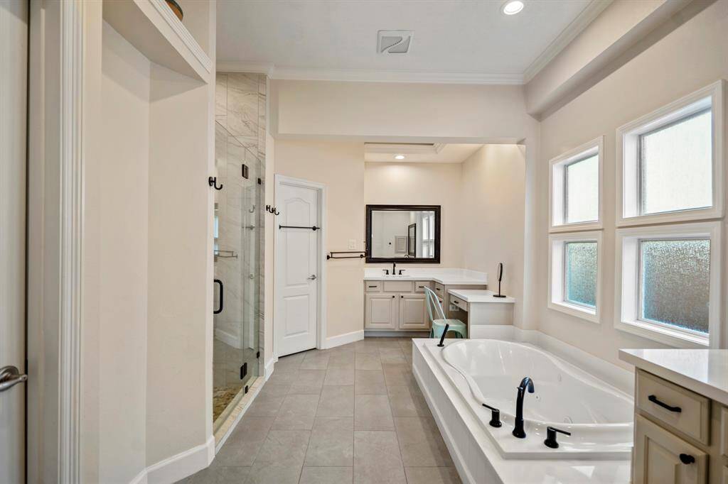 The spa-like ensuite bath features a deep soaking tub, dual vanities, and a sleek makeup station. Frosted windows offer natural light while ensuring privacy.