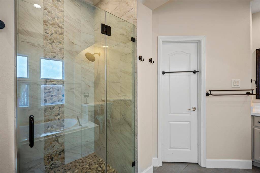 Enjoy a walk-in shower with elegant tile work, river rock flooring, and a rainfall showerhead, creating a luxurious spa experience at home.