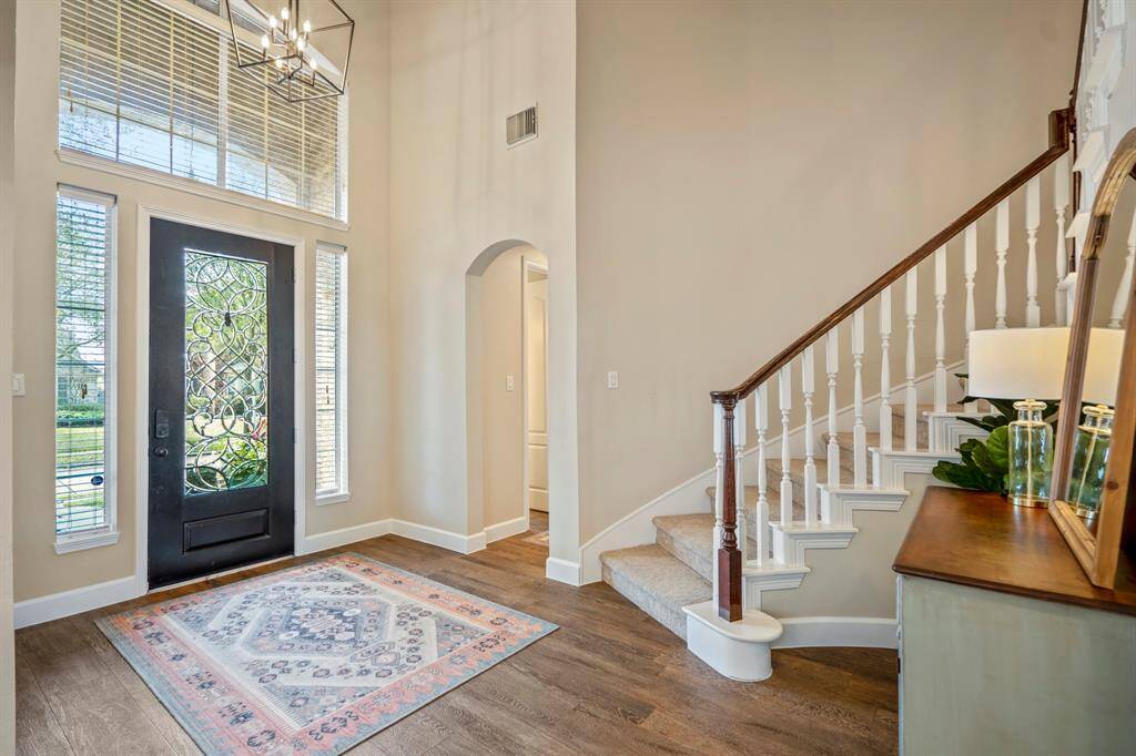 Natural light pours through the decorative glass front door and transom windows, illuminating the elegant curved staircase and inviting foyer.