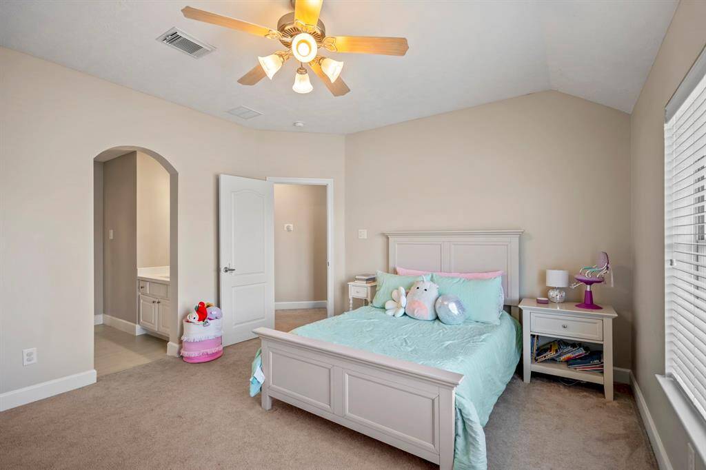 A bright and open bedroom with a vaulted ceiling, plush carpeting, and an ensuite vanity that connects to the shared Hollywood bath for added convenience.