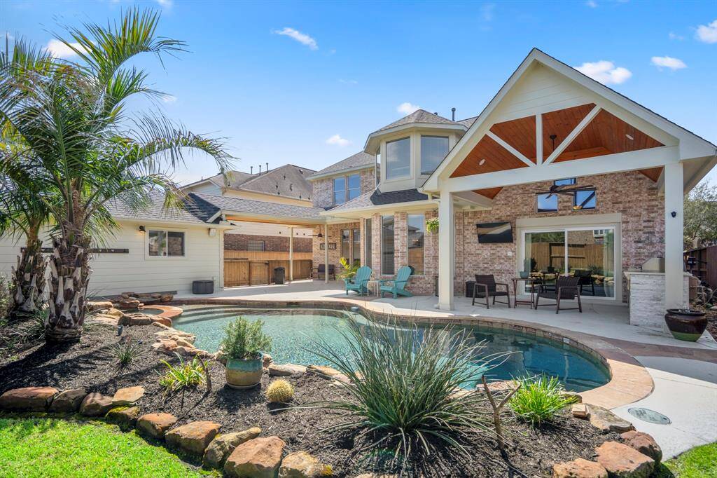 This backyard offers seamless indoor-outdoor living with an extended patio, a shaded lounge area, and direct access to the resort-style pool.