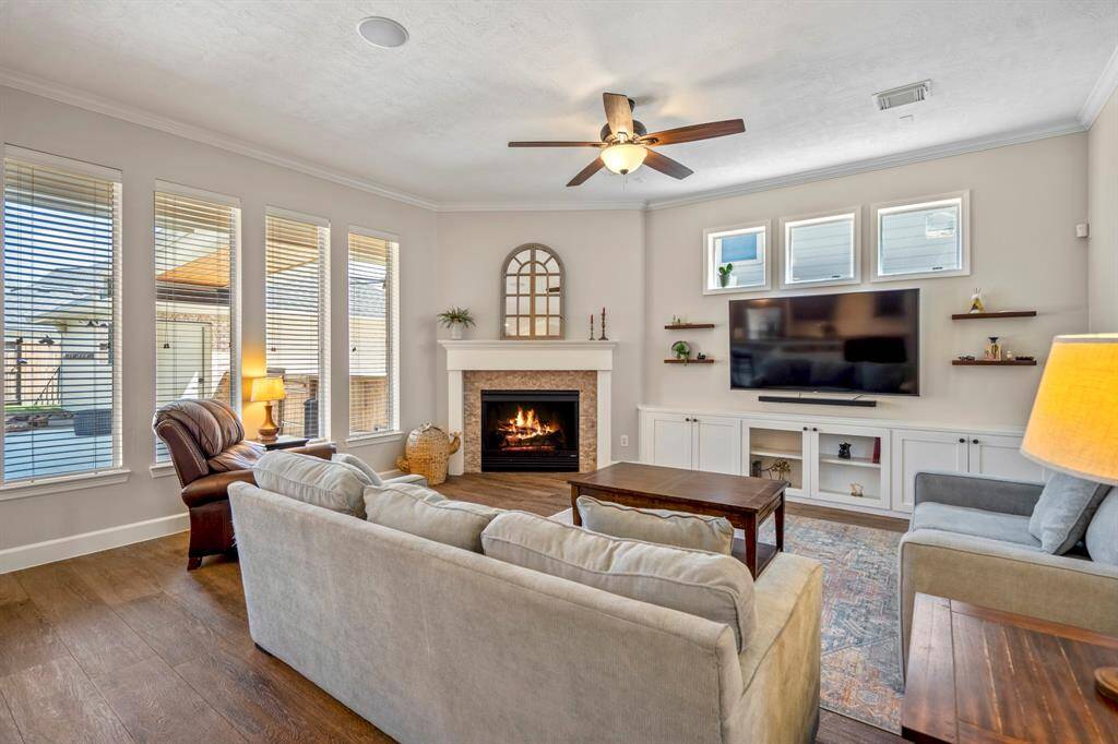 The spacious family room is the heart of the home, offering a cozy fireplace with a stylish stone surround, built-in cabinetry, and a wall of windows overlooking the backyard oasis.