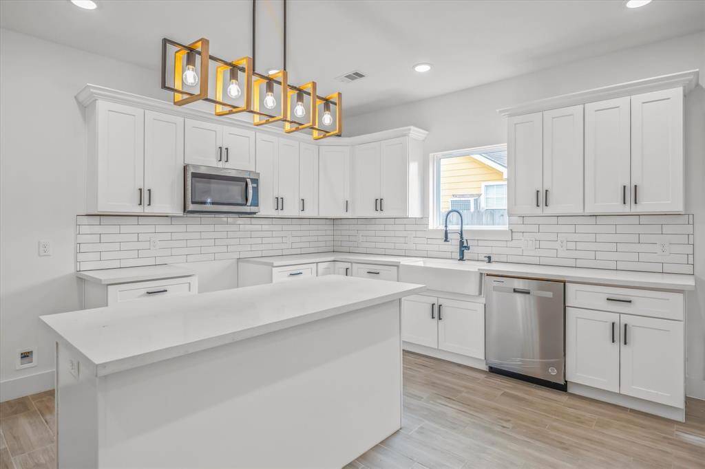 This modern kitchen features a breakfast bar, white shaker cabinets, quartz countertops, subway tile backsplash, farmhouse sink, modern hardware, and a stylish light fixture. A gas range and refrigerator are being installed in the space.
