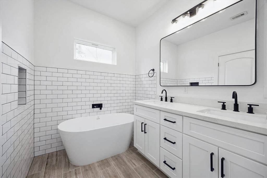 This gorgeous primary bathroom has a subway tiled wall, porcelain soaking tub, double sinks, and chic black hardware to accent the white space.