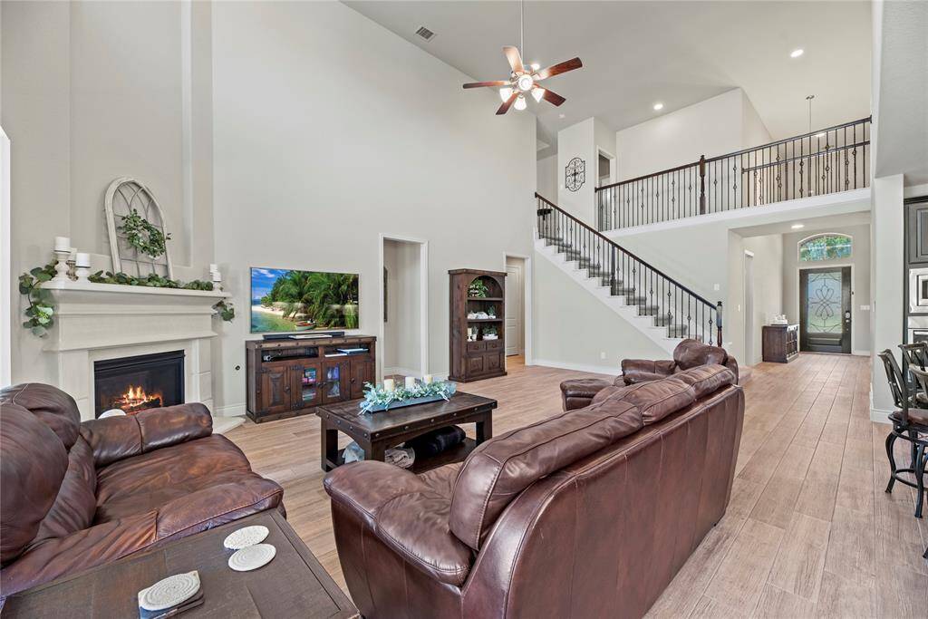 This spacious living room features high ceilings, a cozy fireplace, and elegant wood look tile flooring. It has an open view to the upper level with a stylish staircase. The space is bright and welcoming, ideal for family gatherings and entertaining.