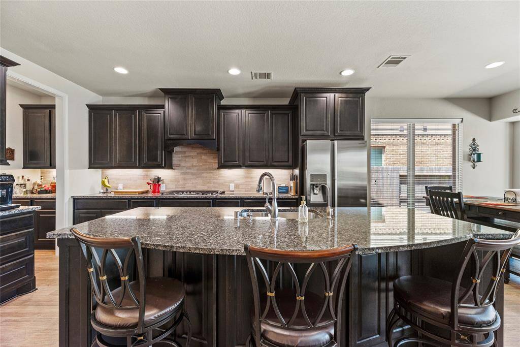 The kitchen features a large granite island with seating, stainless steel appliances and a beautiful backsplash.