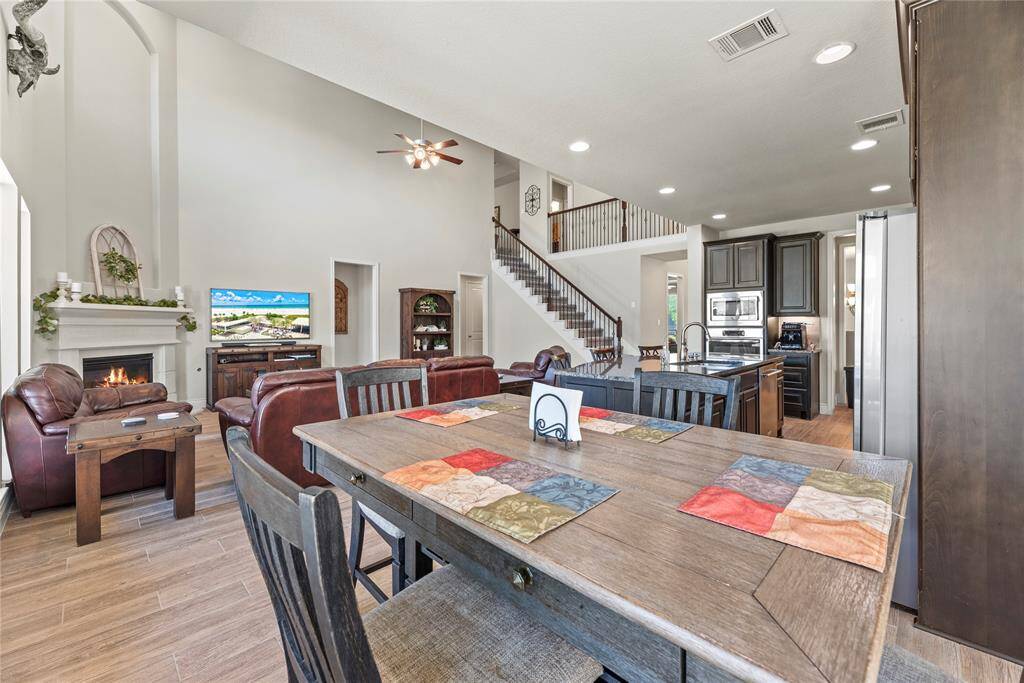 This photo showcases the  spacious open-concept living area with high ceilings, featuring a cozy fireplace, modern kitchen with dark cabinetry and stainless steel appliances, and a dining area.