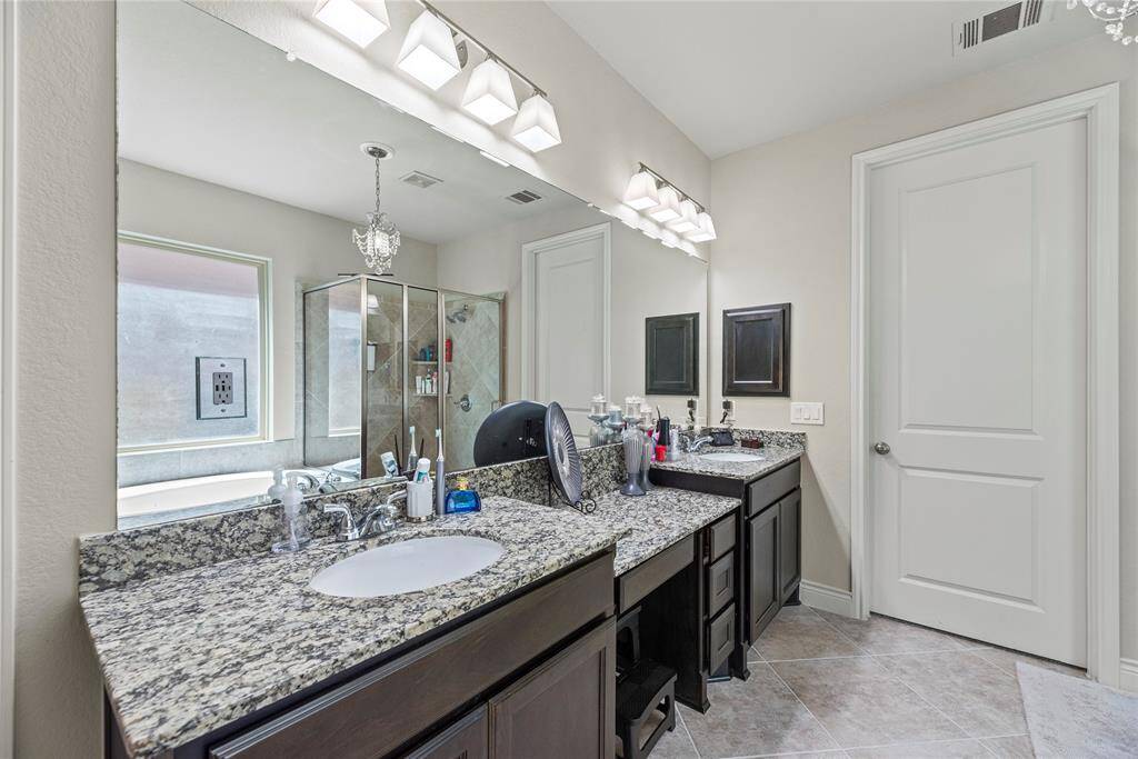 This modern bathroom features dual granite-topped vanities with extra vanity space. It includes elegant lighting and neutral tile flooring, offering a sleek and functional space.