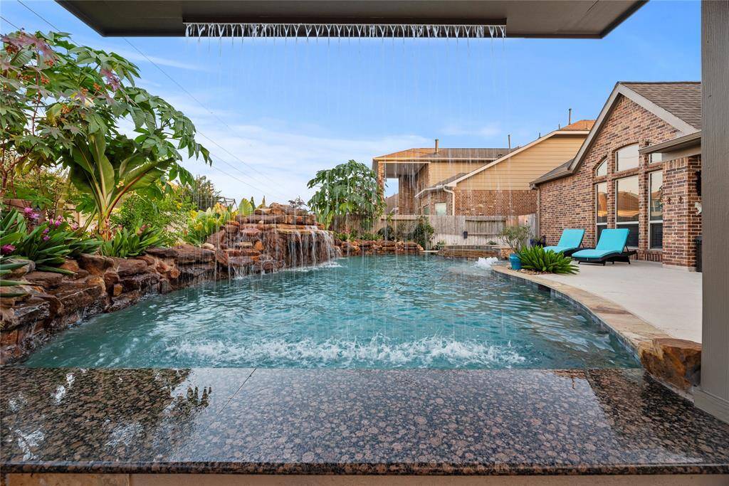 This backyard features a luxurious island inspired pool with a waterfall and lush landscaping. Stand in your sunken outdoor kitchen and Serve up some drinks as your friends and family swim up to the pool bar!
