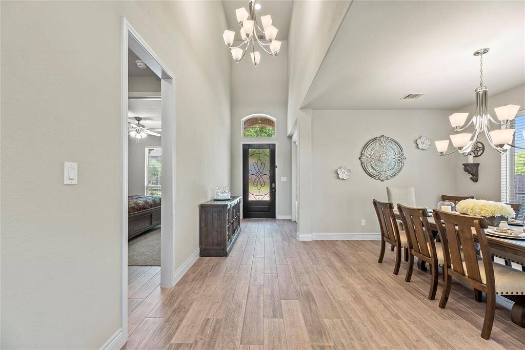 Bright and inviting entryway with high ceilings and elegant light fixtures. The area opens into a spacious dining room with large windows, offering plenty of natural light. The wooden flooring adds warmth and sophistication to the space.