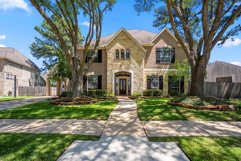 Welcome to 20335 Evergreen Springs Ln, a stunning home nestled in the Windrose community. The beautiful brick and stone facade is framed by two towering trees, offering great curb appeal and a warm welcome.