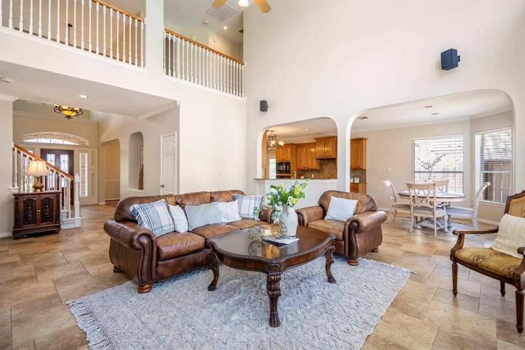 From near the windows, looking back towards the front of the room, you can see the foyer and staircase to the left. Above, the landing overlooks both the living room and foyer, adding to the home's open and airy feel. On the right, arched openings provide a view into the kitchen and breakfast areas, creating a seamless flow throughout the home. The doorway visible behind the couch leads to the convenient half bath.