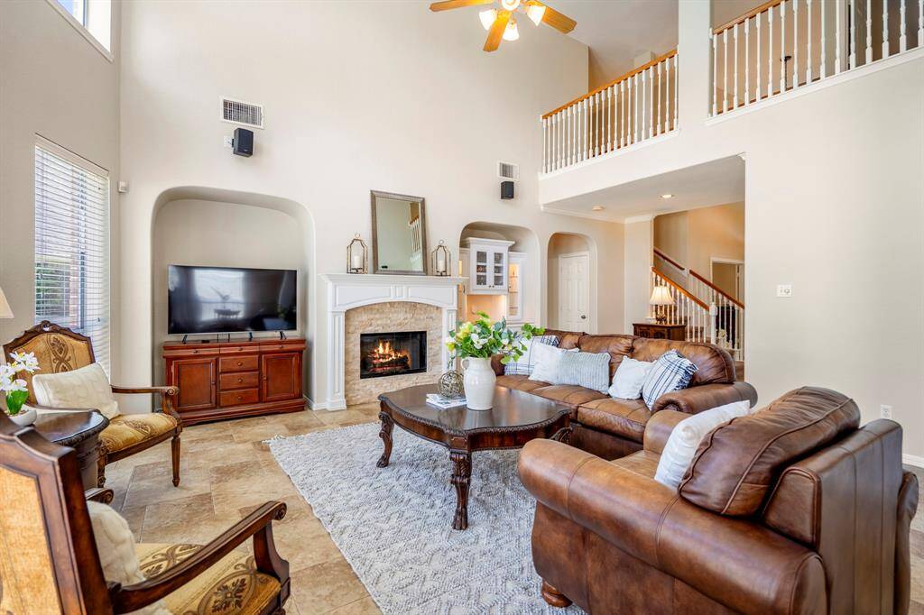 Taken from near the breakfast area, this view of the living room offers another perspective of the fireplace and recessed spaces on either side. An additional archway between the built-ins and the staircase leads to the primary suite. Above, the balcony overlooks both the living room and foyer, adding an open, airy feel to the space.