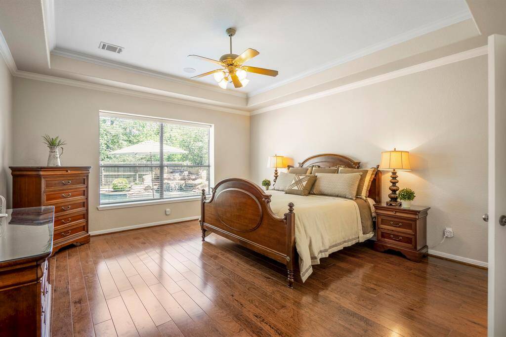 Moving into the primary suite, you'll find a spacious retreat with gleaming wood floors and a large window overlooking the backyard and pool. The tray ceiling, accented with crown molding, adds an elegant touch, making this room feel both luxurious and serene.