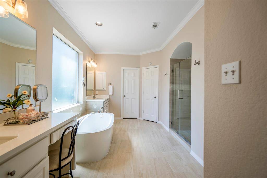 Wow! The primary bath is a true retreat, featuring a standalone tub positioned under a large window, with two sinks—one including a vanity area on the left. To the right, a glass door leads to a spacious walk-in shower. Ahead, you'll find the doors to the expansive walk-in closet (complete with a window) and the linen closet, all designed with luxury and functionality in mind.