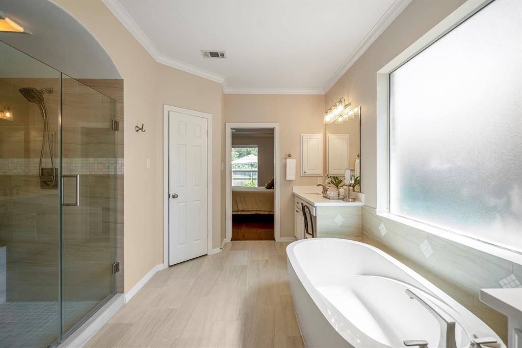 This view offers a closer look at the spacious walk-in shower and a better peek at the standalone tub. To the left, the doorway leads to the private water closet, completing the thoughtful layout of this luxurious primary bath.