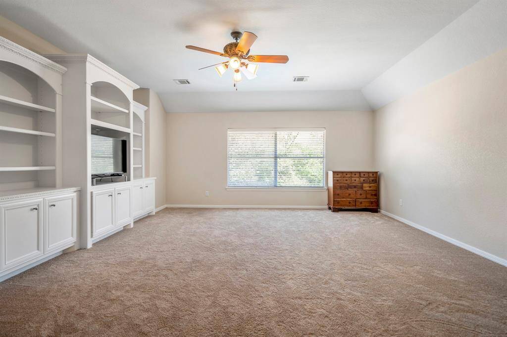 Upstairs, the family room/game room offers vaulted ceilings that add to the sense of space. Built-in shelves provide both style and storage, while a large window overlooks the backyard, offering plenty of natural light and a view of the pool.