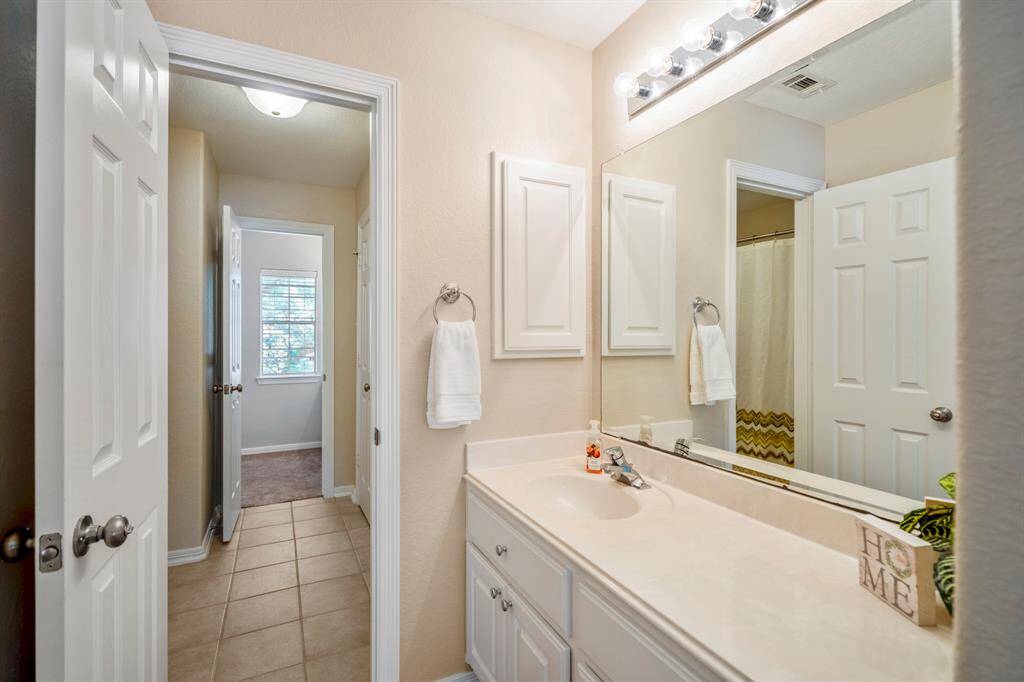 From the second vanity area, this view looks back across the bathroom toward the front of the house, with a clear view of the connecting space leading into the rear bedroom.