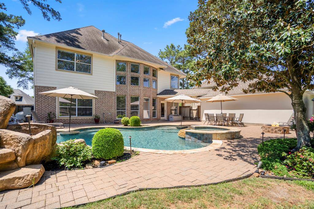 From just behind the waterfall, this view across the pool reveals the spacious patio area, perfect for outdoor entertainment. You can also see the beautiful magnolia tree in the backyard, the inviting fire pit area, and the detached garage, all framed by the tranquil setting of this exceptional home.