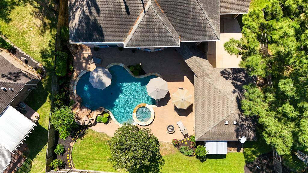 An overhead view of the backyard highlights the thoughtful layout and artistry behind the landscaping and design. From this angle, you can see the detached garage at the bottom right, while the roofline of the covered parking structure on the right side of the home adds a touch of elegance to the overall property.