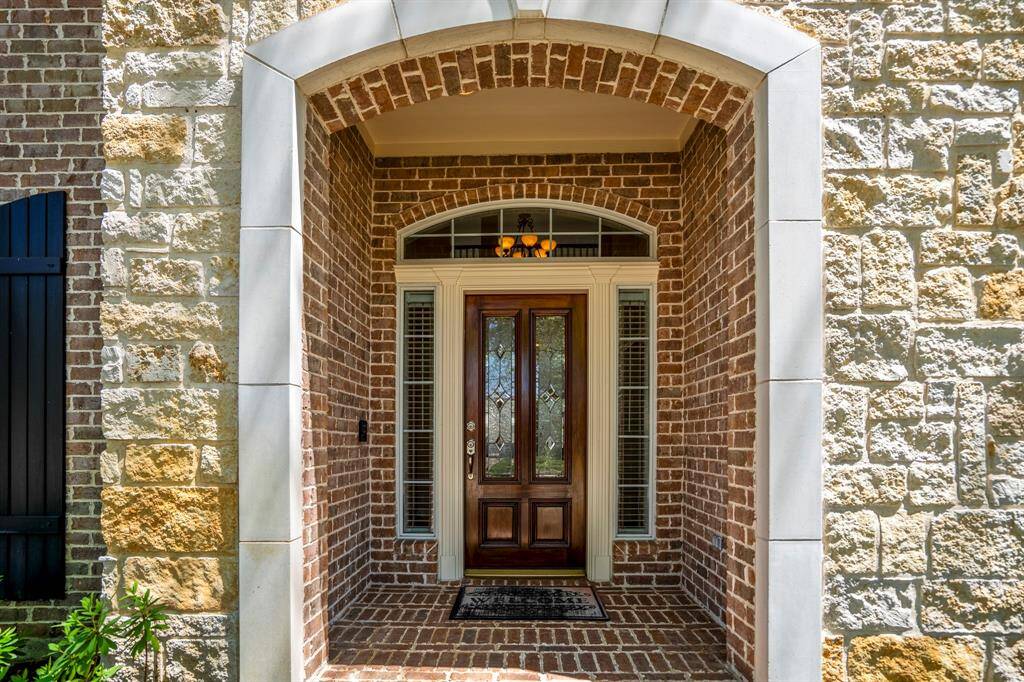 Approaching the front porch, you're greeted by a beautiful stone archway and red brick exterior. The wood front door, with its decorative glasswork and detailed wood trim, sets the tone for the custom finishes and impressive touches found throughout the interior.