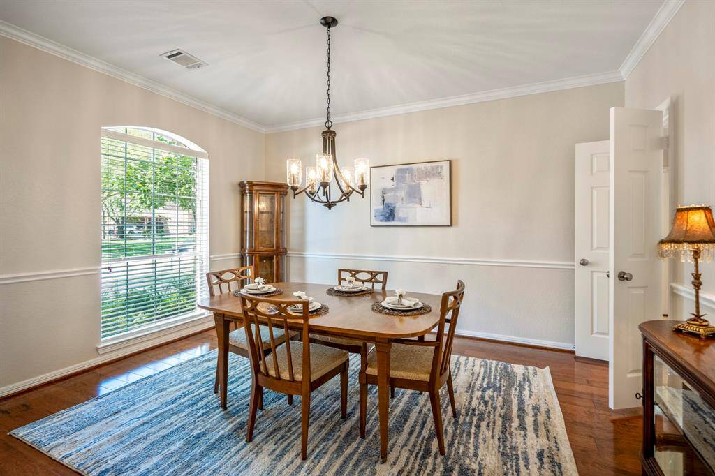 Moving across the foyer into the formal dining room, you'll find gleaming wood floors and a large window overlooking the front yard. The sleek, modern chandelier adds a touch of elegance, while the chair railing and crown molding provide sophisticated detailing. Double doors lead into the kitchen, making this space perfect for both intimate meals and entertaining.
