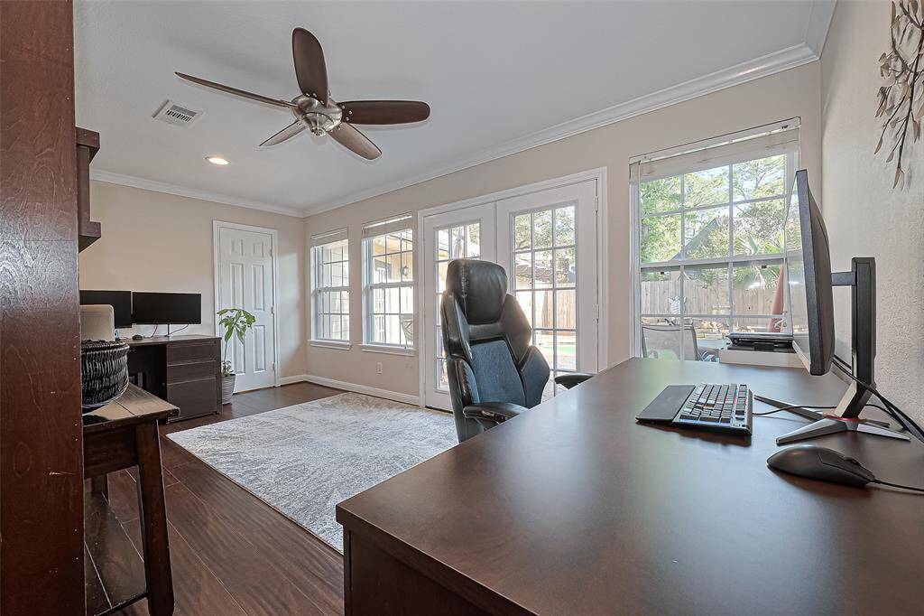 This versatile space, currently used as a home office, is filled with abundant natural light thanks to a wall of windows and elegant French doors that offer a serene view of the backyard.