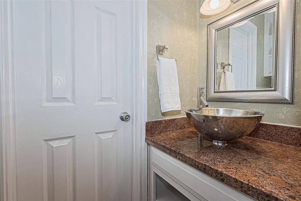 Just off the main living area, you’ll find this beautifully appointed powder room featuring a striking vessel sink that adds a touch of modern elegance. The granite countertop offers a rich, polished surface, while the decorative framed mirror and soft overhead lighting create a refined, welcoming feel for your guests.