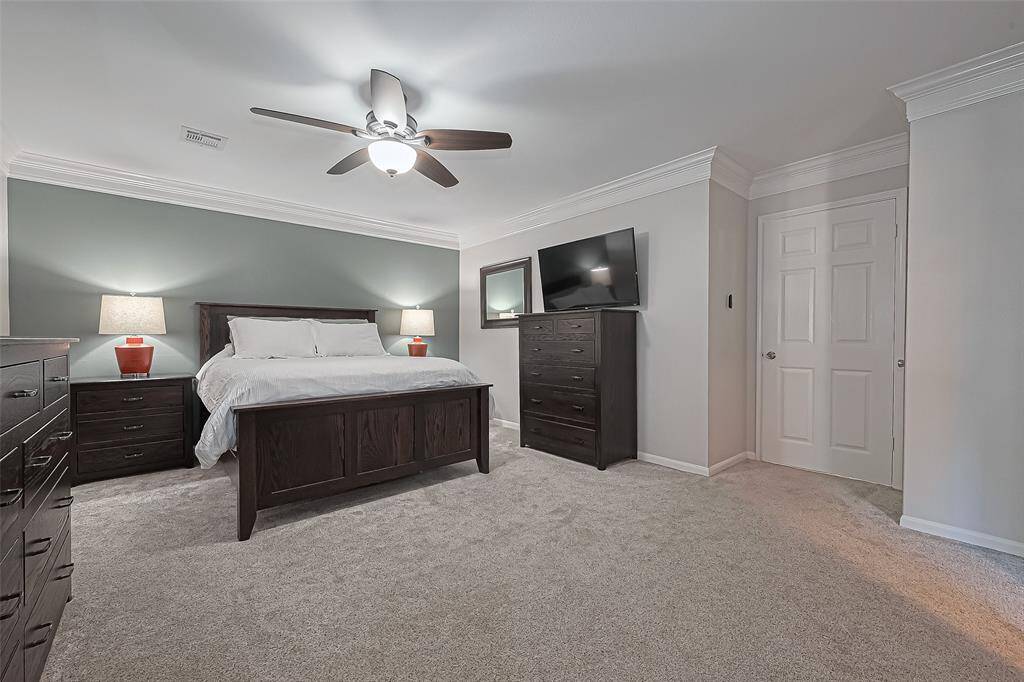 The spacious primary suite offers a serene retreat with plush carpet, elegant crown molding, and a relaxing ceiling fan to enhance your comfort day or night.