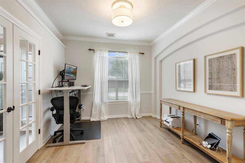 This bright home office features a large window providing natural light. It has hardwood floors and French doors, offering a spacious and inviting work environment.
